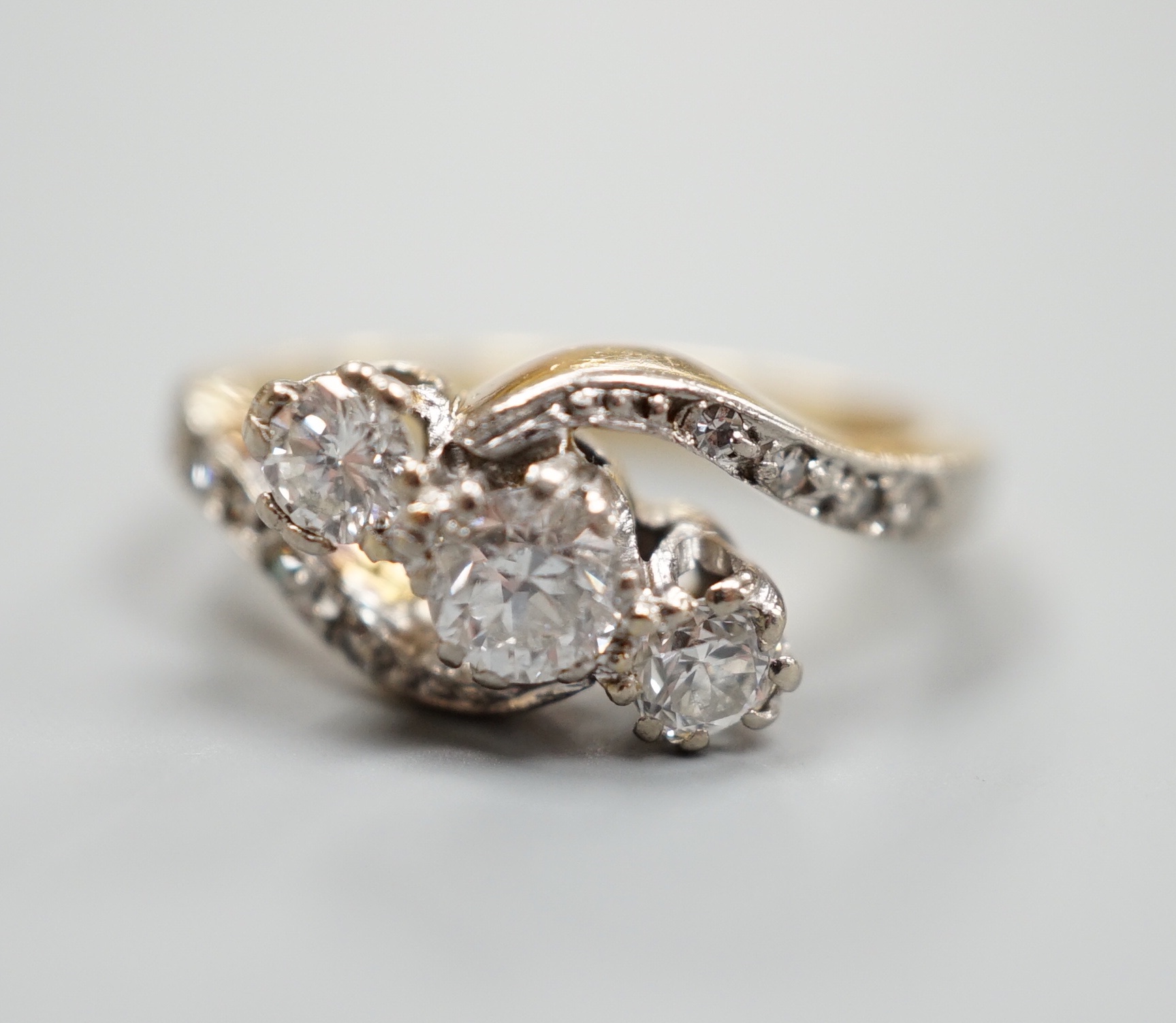 A yellow metal and three stone diamond set crossover ring, with diamond set shoulders, size I, gross 4.6 grams.